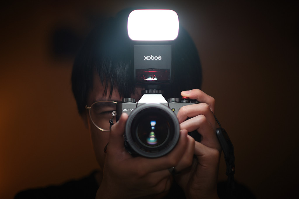 Self-portrait of me using my mirrorless camera with a dedicated flash on a mirror 