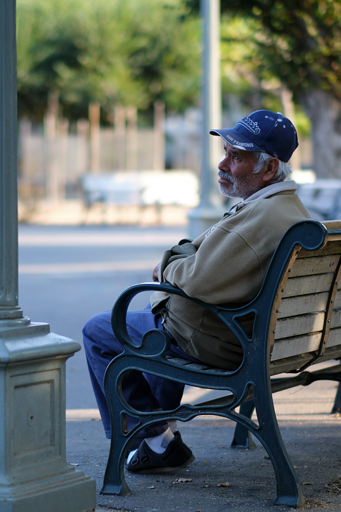 An older man sitting on a park bench with a wistful gaze