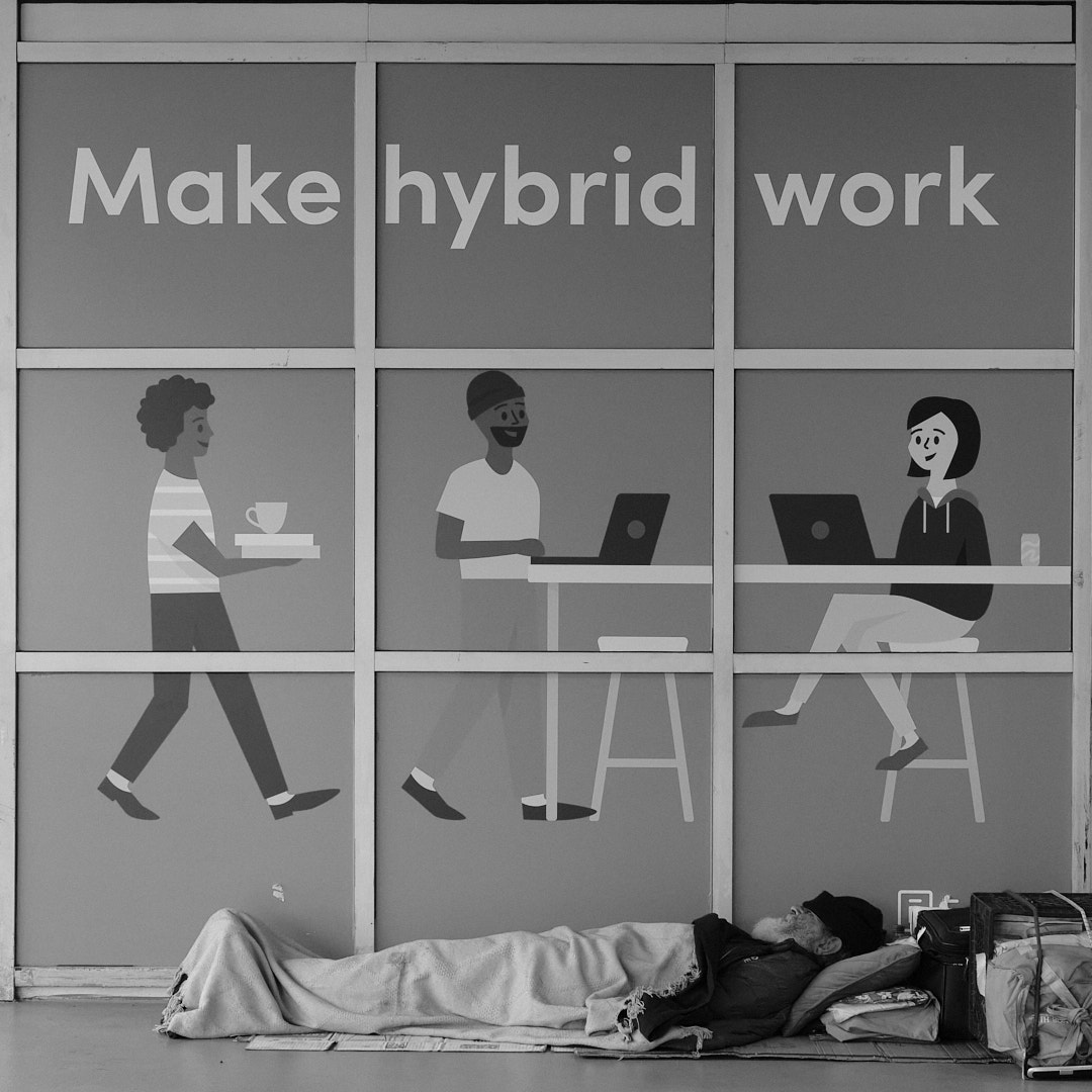 Homeless man sleeping under an advertisement about hybrid work